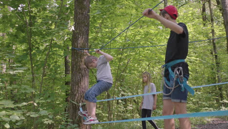 Children-on-a-summer-camp-hike-are-moving-along-the-ropes-with-the-help-of-a-guide-who-teaches-children-rock-climbing-and-tourism.-A-boy-in-the-forest-overcomes-a-rope-barrier